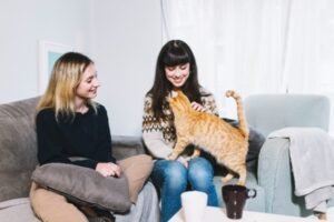 Two girls sitting and having fun with a cat.